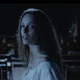 A woman in a white nightgown looks over her shoulder in fear.